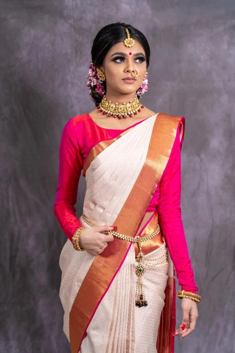 Traditional ivory and gold saree draping with a vivid pink blouse