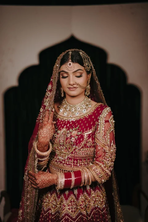 Bride in a red lehenga with carefully arranged bridal veil and gold jewellery